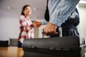 A plumber with a toolbox shakes a customer’s hand