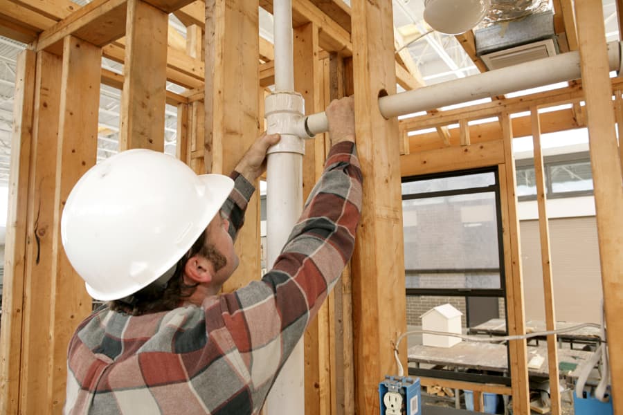 A plumbing contractor connects pipes in a new wall