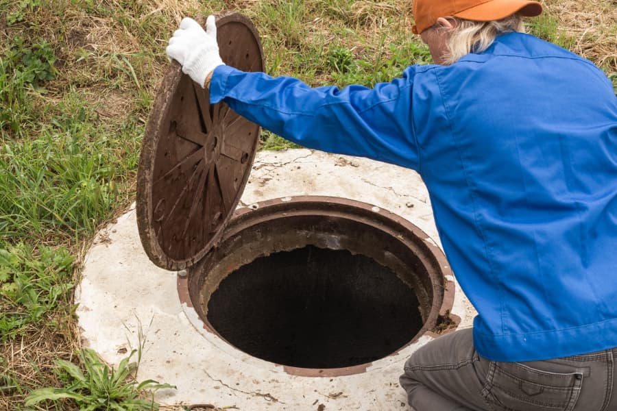 A maintenance worker opens a septic tank hatch