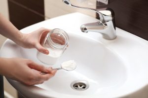 Hand pouring baking soda down bathroom sink