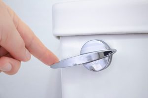 Person pushing toilet handle to flush wastewater